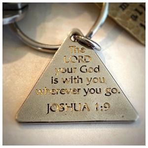 A triangular keychain engraved with the Bible verse Joshua 1:9